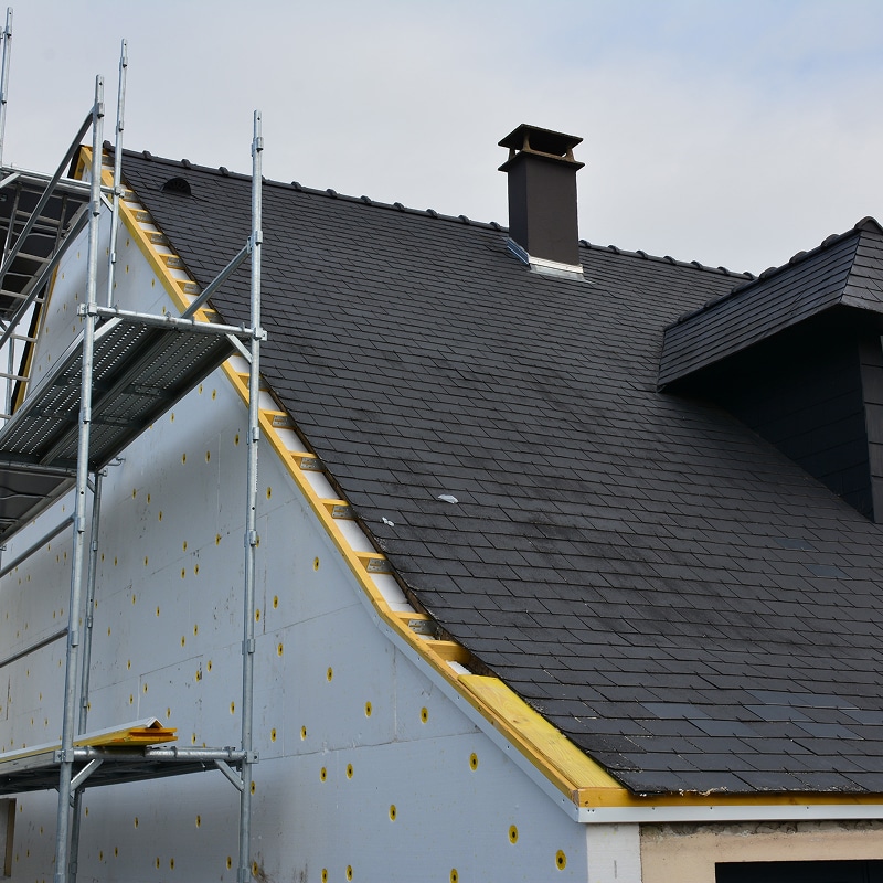 Isolation et Rénovation de Façade en Pleine Œuvre Rénovation de façade en cours : isolation thermique extérieure avec laine minérale et bardage en tôle ondulée rouge, échafaudage en place.