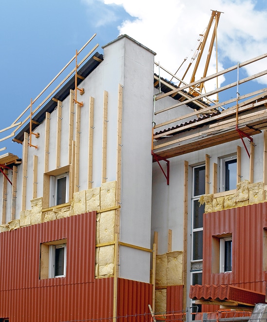 Isolation et Rénovation de Façade en Pleine Œuvre Rénovation de façade en cours : isolation thermique extérieure avec laine minérale et bardage en tôle ondulée rouge, échafaudage en place.