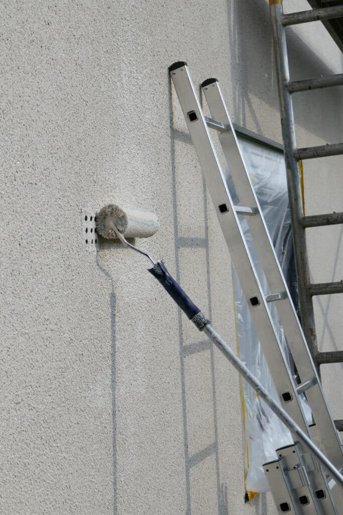 Rénovation Façade : Application peinture sur mur crépis. Rénovation de façade : un rouleau de peinture travaille sur un mur en crépis près d'une échelle et d'un échafaudage métallique.